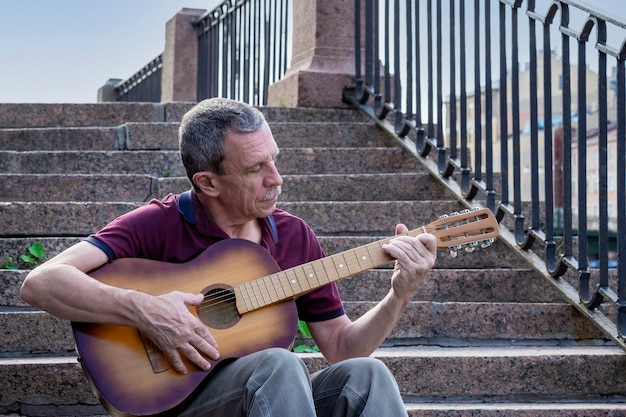 L'anziano adulto in età pensionabile suona una chitarra acustica in città