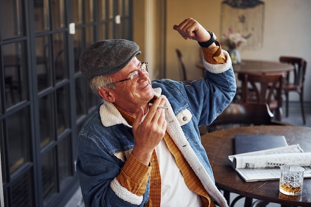 L'anziano elegante in abiti alla moda e con gli occhiali si siede al bar con sigaretta e parla.