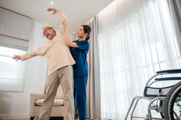 L'anziano uomo anziano si diverte ad allenarsi con il fisioterapista per le braccia tese a casa, il paziente asiatico del fisioterapista infermieristico aiuta gli anziani a esercitare l'allungamento del braccio, la riabilitazione del concetto di disabile