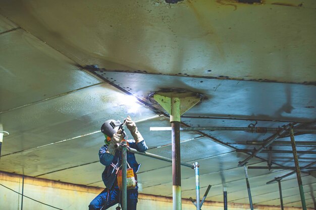 L'arco di metallo del lavoratore maschio di saldatura fa parte dell'olio del serbatoio della costruzione della conduttura dell'ugello del serbatoio del macchinario all'interno di spazi ristretti