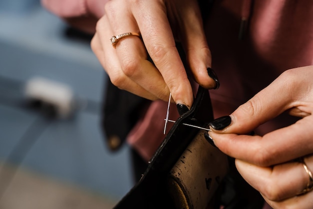 L'artigiano cuce la vera pelle utilizzando ago e filo per la creazione di prodotti in pelle naturale Attrezzature per la produzione di vera pelle in officina Processo di cucitura della vera pelle