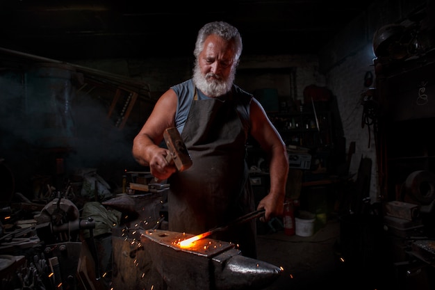 L'artigiano fabbro in grembiule lavora nella bottega del fabbro