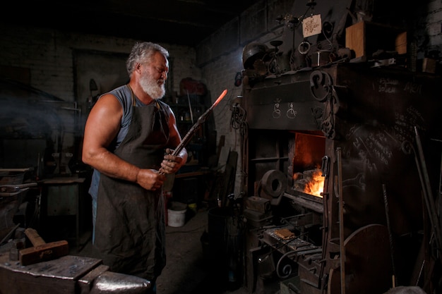 L'artigiano fabbro in grembiule lavora nella bottega del fabbro