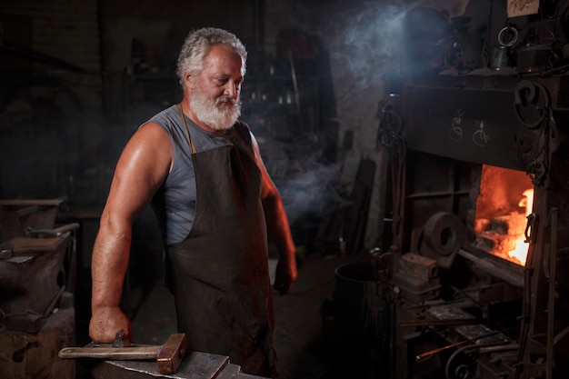 L'artigiano fabbro in grembiule lavora nella bottega del fabbro