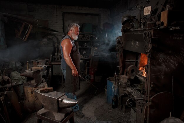 L'artigiano fabbro in grembiule lavora nella bottega del fabbro