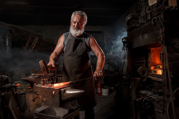 L'artigiano fabbro in grembiule lavora nella bottega del fabbro