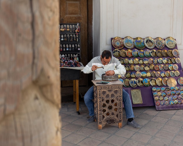 L'artigiano realizza un piatto di souvenir in metallo decorativo al mercato nella città vecchia di Bukhara, in Uzbekistan