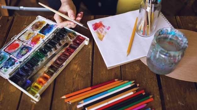 L'artista della giovane donna disegna il pictrure con le pitture ad acquerello e il primo piano dei colori di miscelazione del pennello