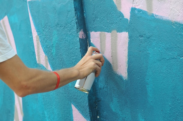 L'artista di strada con uno spray disegna graffiti colorati sul muro di cemento