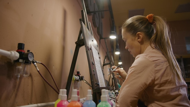 L'artista donna impara a dipingere con l'aerografo con carta colorante acrilica e cavalletto all'interno