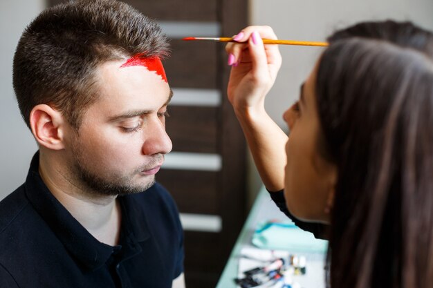 L'artista ragazza dipinge sul viso di un uomo