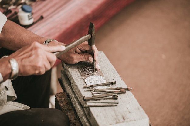 L'artista senior tailandese del nord handcraft l'argento dell'intagliatore con il martello e lo scalpello per il mestiere di arte d'argento di stile della cultura a Chiang Mai, Tailandia.
