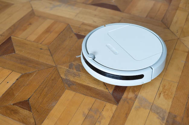 L'aspirapolvere robot si trova sul pavimento in parquet chiaro, vista dall'alto.