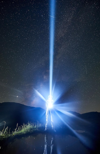 L'astronauta che indossa una tuta spaziale dirige un raggio di luce nel cielo con l'aiuto di una lanterna nella notte in montagna