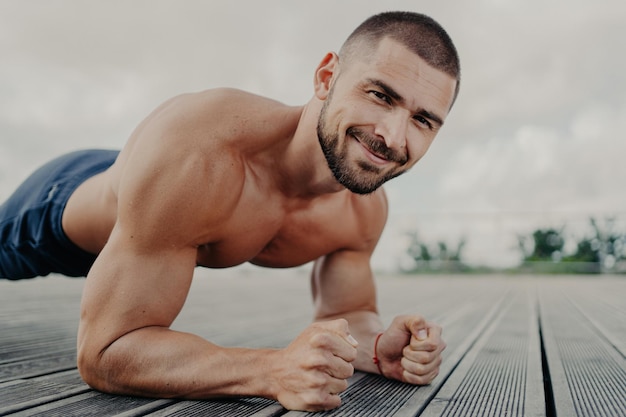 L'atleta barbuto si allena all'aperto fa esercizi di plank e pushup si concentra sullo sviluppo muscolare e dimostra i suoi bicipiti