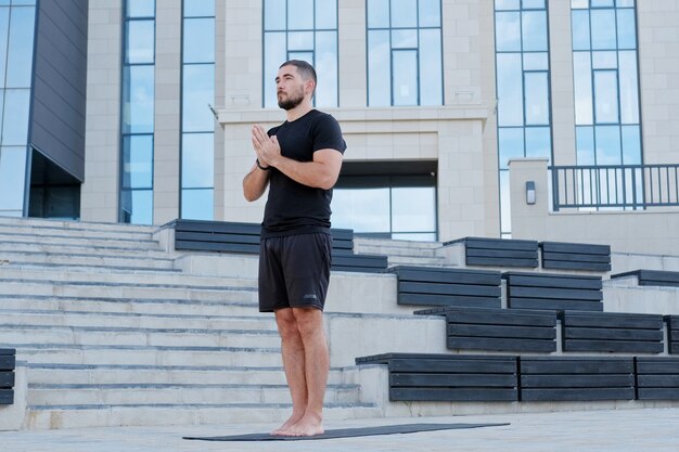 L'atleta dell'uomo in abiti sportivi neri pratica la posizione di preghiera degli esercizi di yoga. Mani nella postura del namaste.