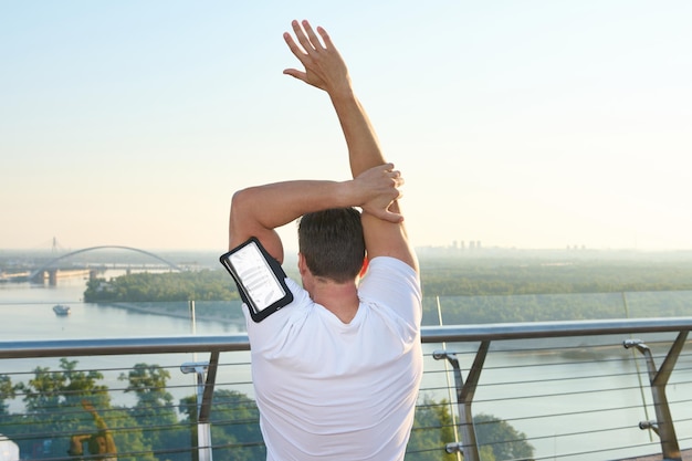 L'atleta fa sport in un ambiente urbano Vista posteriore di un atleta che si esercita sul ponte della città riscaldandosi e allungando il corpo durante un allenamento mattutino all'aperto all'alba