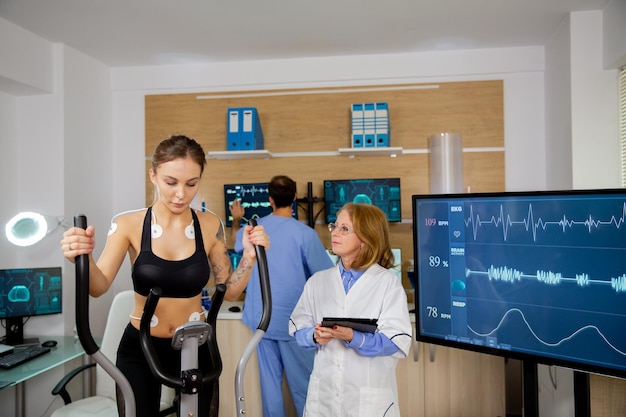 L'atleta femminile che fa uno sforzo fisico sullo stepper e il medico con il tablet in mano la inseguono. Test sportivi