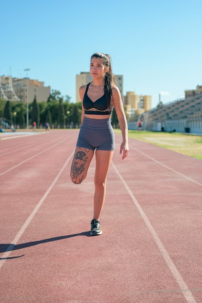 L'atleta femminile con tatuaggi esegue lo stretching su una pista da corsa