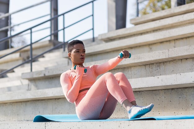 L'atleta femminile si esercita con i manubri vicino allo stadio, la donna afroamericana scuote la stampa e i muscoli del pavimento pelvico al mattino allo stadio sportivo