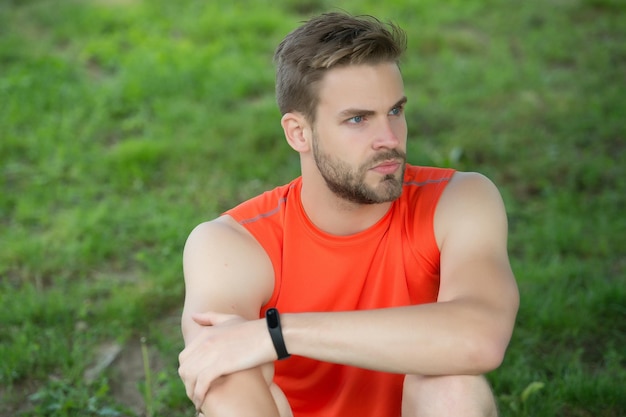 L'atleta indossa il braccialetto pedometro a portata di mano L'uomo atletico si rilassa sull'erba verde Controllare i risultati dell'allenamento Le tecnologie facilitano l'allenamento Uomo muscoloso in estate Tenere d'occhio il tempo