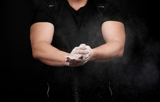 L'atleta muscoloso in uniforme nera si strofina le mani con magnesia sportiva bianca e asciutta