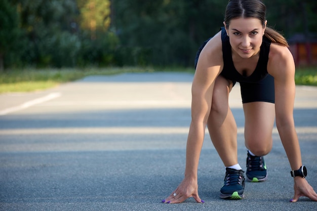 L'atleta si trova nella posizione di partenza per correre sull'asfalto sotto i luminosi raggi del sole del tramonto