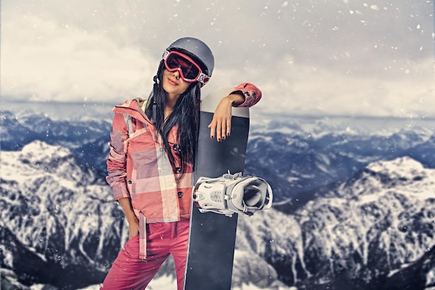 L'attraente donna sportiva tiene lo snowboard in una sessione fotografica in alta montagna.