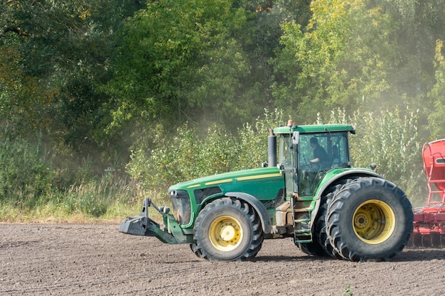 L'attrezzatura per la semina lavora sul campo in una giornata estiva secca Stagione per la semina dei cereali Un agricoltore alla guida di un trattore con un coltivatore