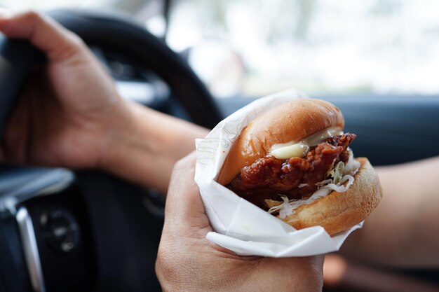 L'autista della donna asiatica tiene e mangia l'hamburger in macchina pericoloso e rischia un incidente