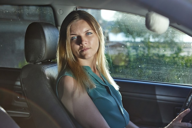 L'autista donna con i capelli biondi è seduta sul sedile dell'automobile durante la guida.