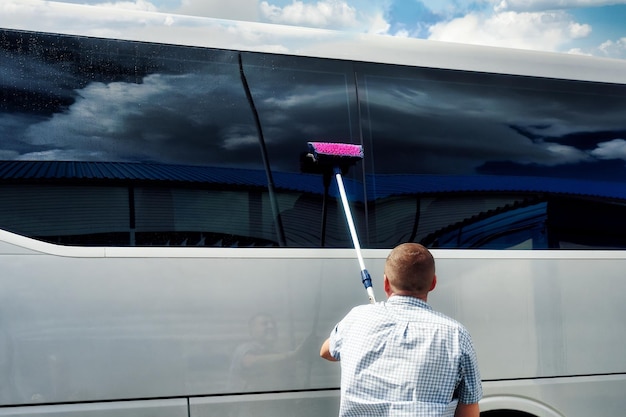L'autista spazzola i grandi finestrini oscurati dell'autobus nei giorni estivi Cura e manutenzione delle apparecchiature