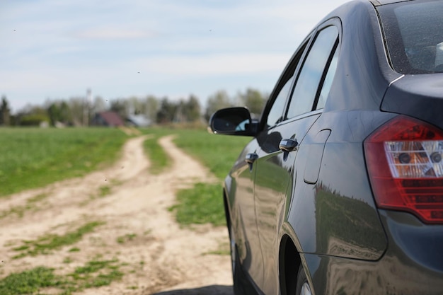 L'auto è parcheggiata nel campo L'auto sta percorrendo la strada rurale verso la casa L'auto è grigia nel prato davanti alla strada di campagna