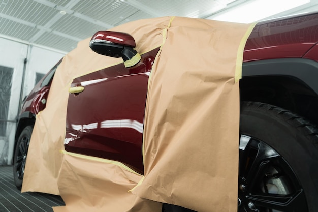 L'auto ricoperta di nastro adesivo e carta è nella cabina per la verniciatura prima della riverniciatura o della lucidatura