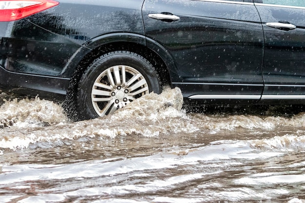 L'auto sta attraversando una pozzanghera sotto una forte pioggia Spruzzi d'acqua da sotto le ruote di un'auto Inondazioni e acqua alta in città