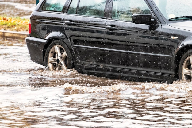 L'auto sta attraversando una pozzanghera sotto una forte pioggia Spruzzi d'acqua da sotto le ruote di un'auto Inondazioni e acqua alta in città