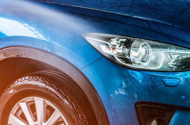 L'auto SUV compatta blu con sport e design moderno si sta lavando con acqua. Concetto di affari di servizio di cura dell'automobile. Auto coperta di gocce d'acqua dopo la pulizia con acqua nebulizzata ad alta pressione