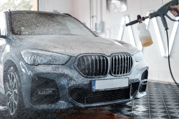 L'auto viene lavata in un lavandino professionale L'uomo lava l'auto con schiuma Dettaglio