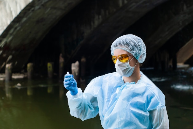 L'ecologa o l'epidemiologo femminile esegue l'analisi dell'acqua in provetta in un fiume della città sotto il vecchio ponte