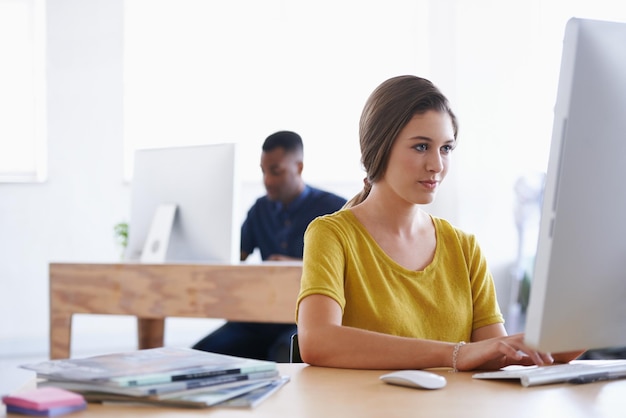 L'efficienza è tutto Una giovane donna che lavora alla sua scrivania con il suo collega in background