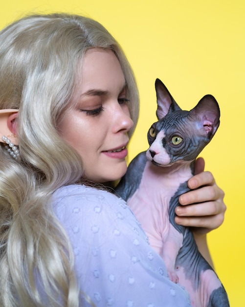 L'elfo cosplay di giovane donna in abito blu tiene il gattino Sfinge nelle mani guardandolo con amore