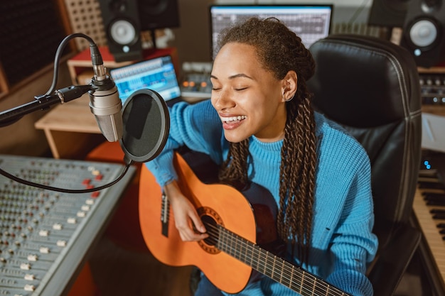 L'entusiasta cantante multietnica suona la chitarra e la canzone dei record canta nel microfono nella musica