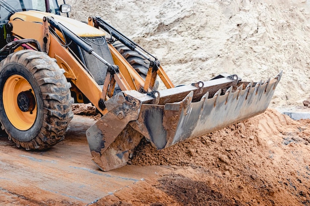 L'escavatore riempie la fossa con la benna anteriore. Sposta il terreno intorno al cantiere. Avvicinamento. Macchine edili pesanti.