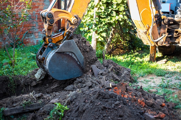 L'escavatore scava il terreno con un grande secchio sul terreno per posare un sistema di approvvigionamento idrico.