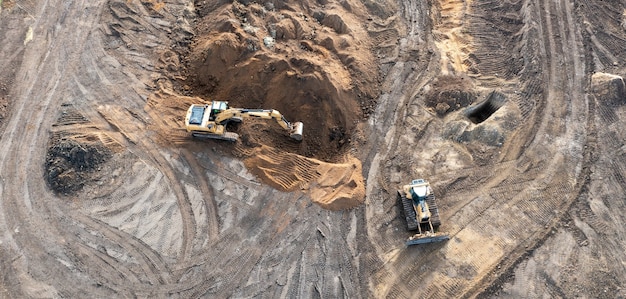 L'escavatore scava una trincea sotto le fondamenta e il bulldozer sgombra il terreno. Vista dall'alto di un cantiere