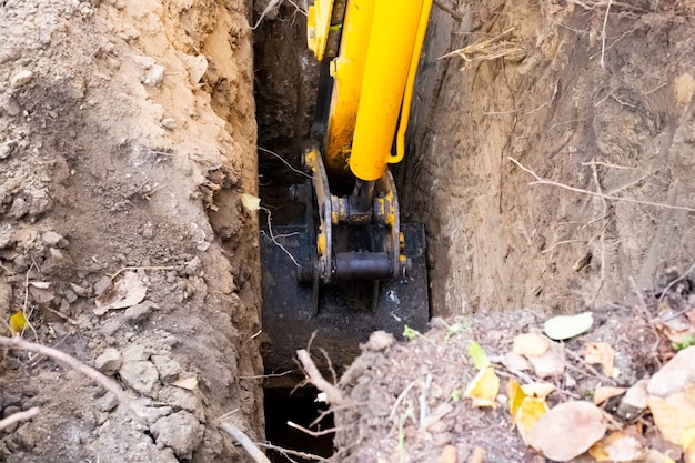 L'escavatore spala la terra dalla fossa sotto la fossa settica con un secchio. Lavorare la macchina con il terreno.