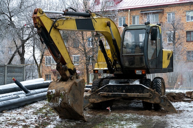 L'escavatore sta lavorando in cantiere per sostituire la condotta in inverno Scavo di buche per la posa di nuove tubazioni per il riscaldamento centralizzato in una zona residenziale
