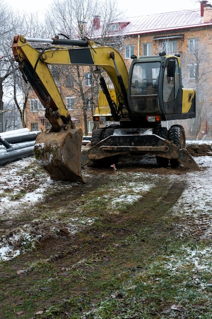 L'escavatore sta lavorando in cantiere per sostituire la condotta in inverno Scavo di buche per la posa di nuove tubazioni per il riscaldamento centralizzato in una zona residenziale