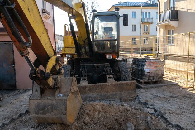 L'escavatore sta lavorando in cantiere per sostituire la condotta in inverno Scavo di buche per la posa di nuove tubazioni per il riscaldamento centralizzato in una zona residenziale