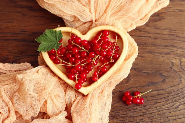 L'estate è il momento delle bacche di vitamina ribes rosso in una ciotola di legno a forma di cuore su un tovagliolo arancione vista dall'alto spazio per il testo